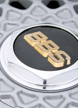 Load image into Gallery viewer, Close-up of a gold and black BBS logo on a high polished wheel center cap with metallic silver and chrome details.