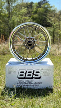 Load image into Gallery viewer, BBS LM471/474 wheel for Porsche with 5x130 bolt pattern, shown on a branded box, highlighting two-piece forged design in grassy outdoor setting.
